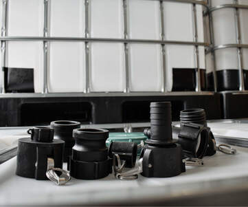 Adaptrar med kamlock-koppling och slangkoppling som ligger på en IBC tank. I bakgrunden syns flera IBC.