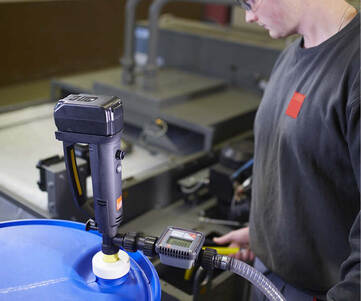 En person som pumpar vätska från ett plastfat med en batteridriven fatpump.